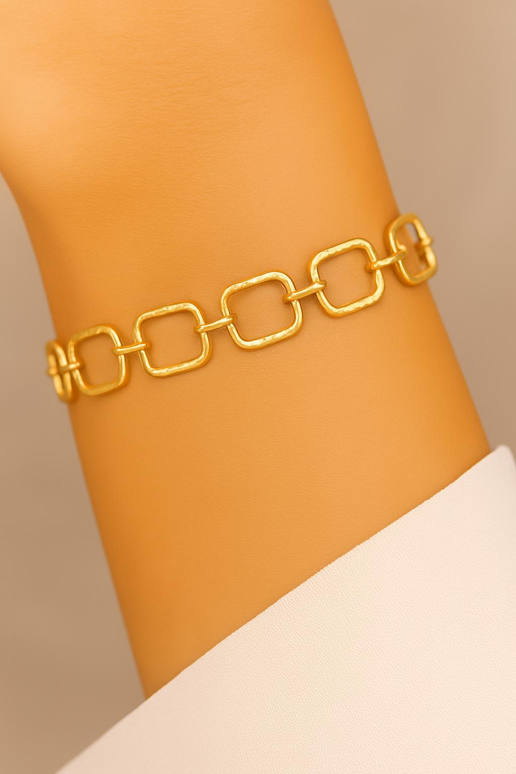 Gold chain bracelet on a wrist against a beige background