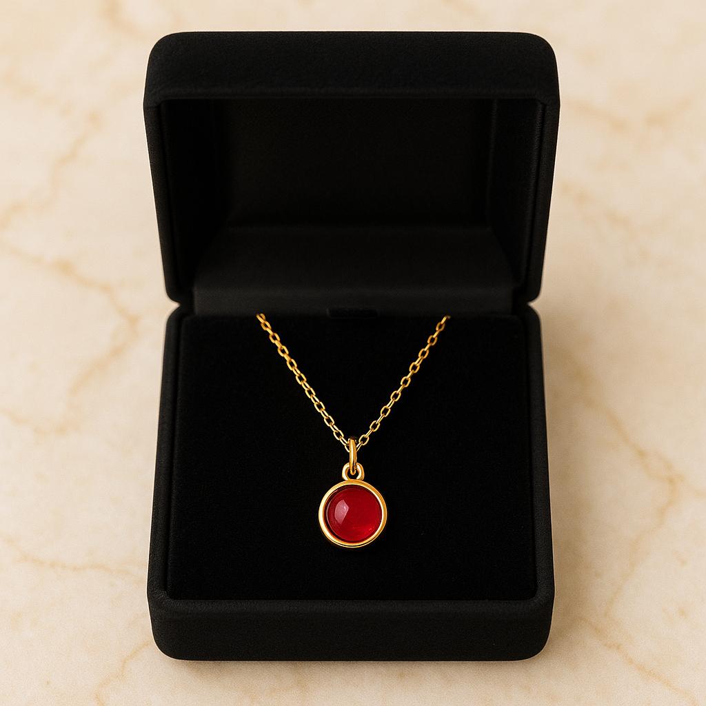 Gold necklace with a red pendant in a black jewelry box on a beige marble background