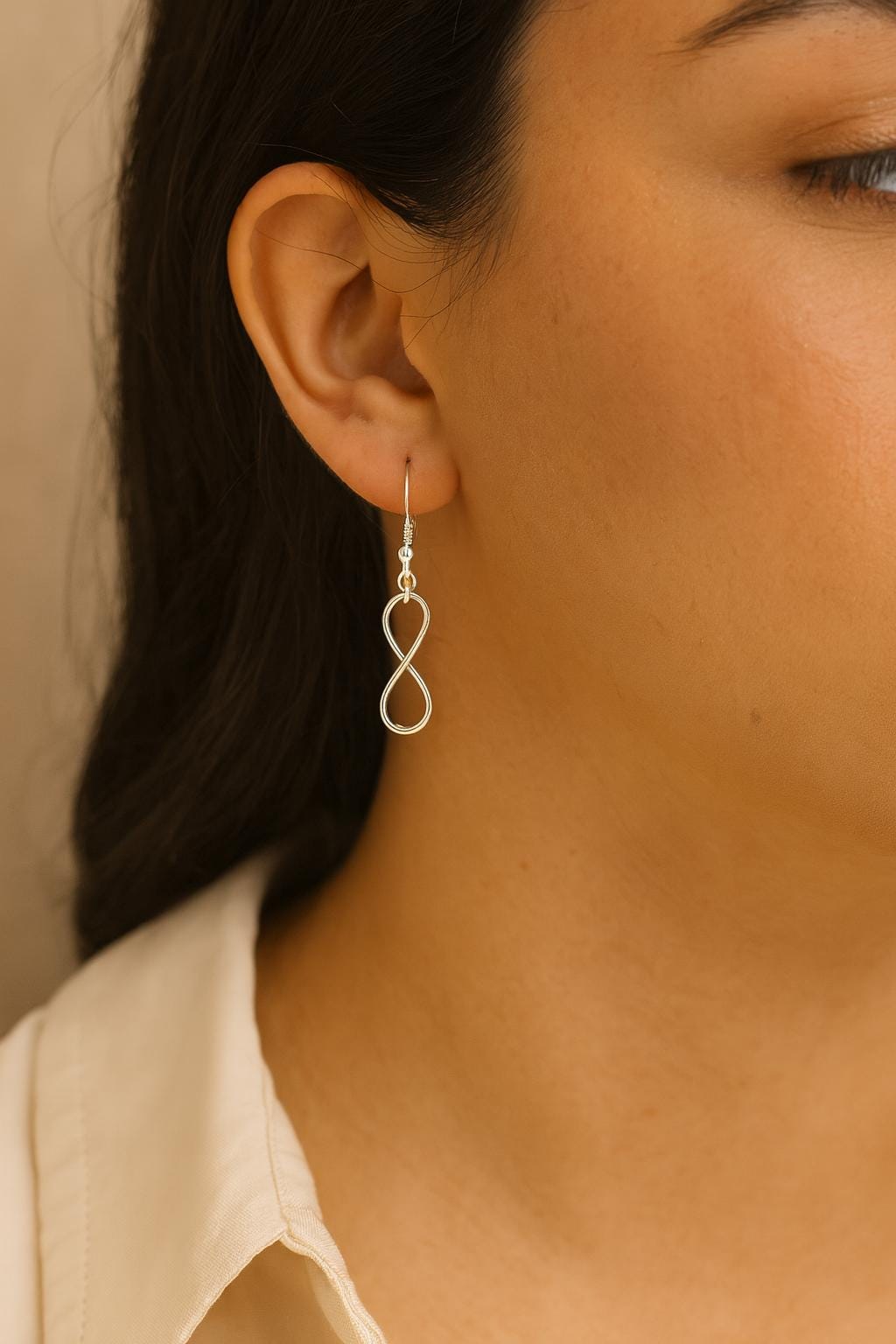 Close-up of a person wearing a silver infinity symbol earring against a neutral background