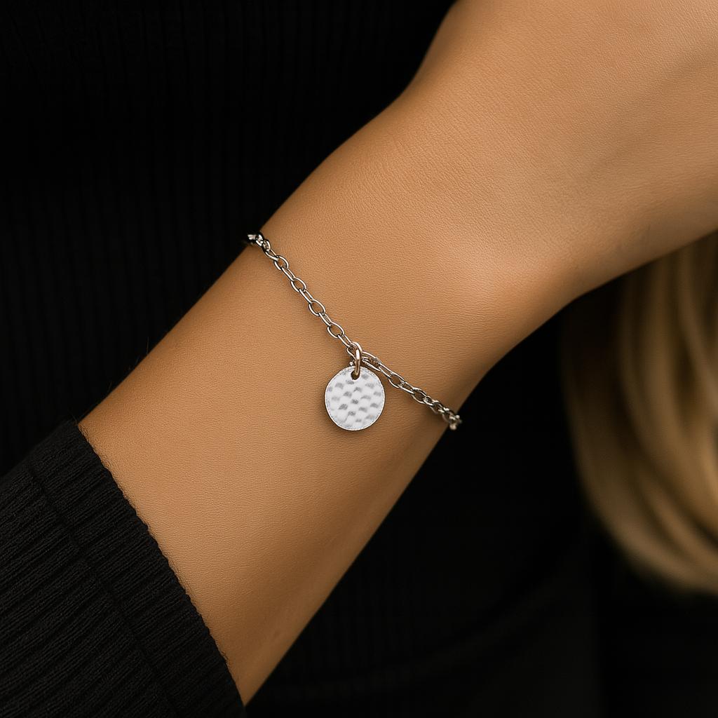 Silver bracelet with a round charm on a wrist against a dark background