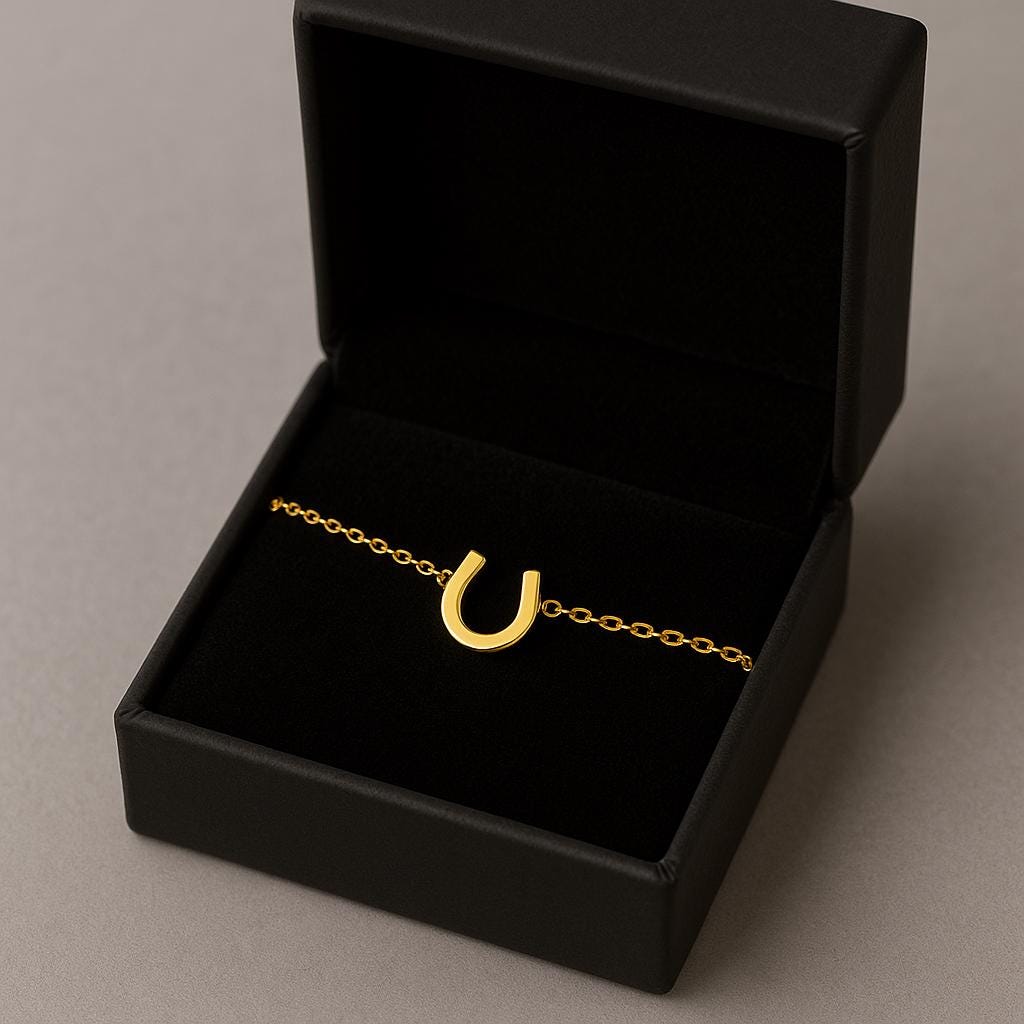 Gold bracelet with a horseshoe charm in an open black jewelry box on a gray background