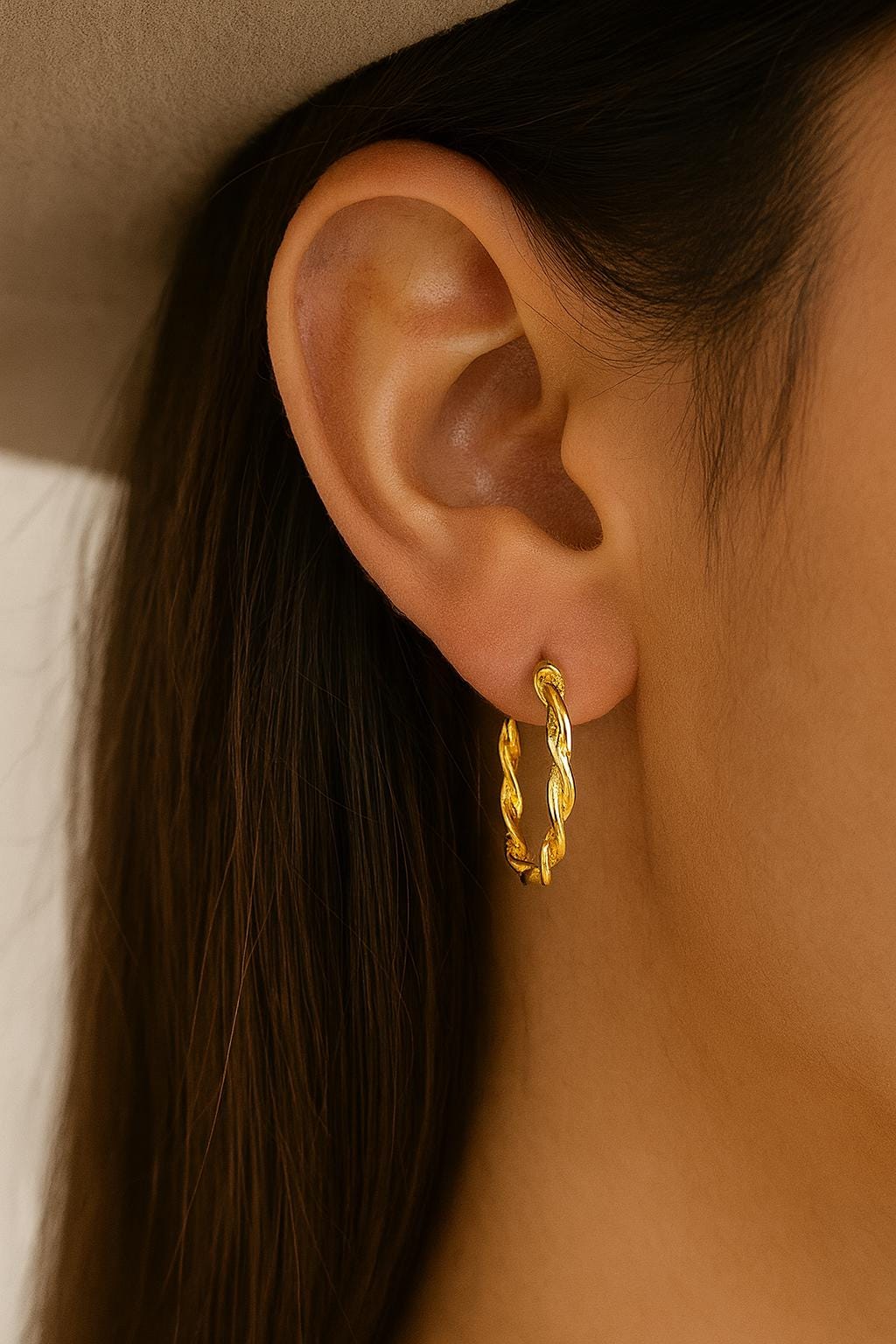 Close-up of an ear wearing a gold hoop earring with a neutral background
