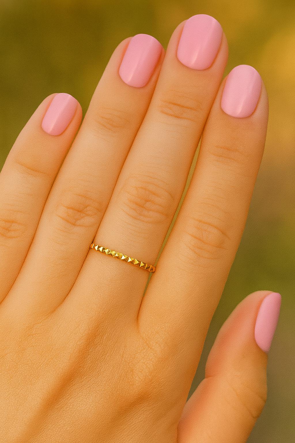 Hand with pink nail polish and a gold ring on a blurred natural background