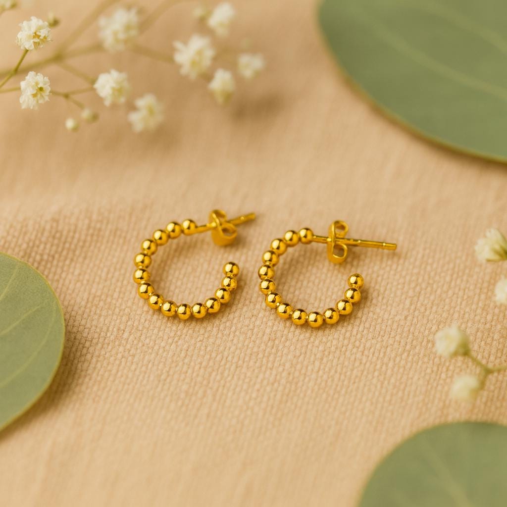 Gold hoop earrings on a beige fabric background with green leaves and small white flowers.