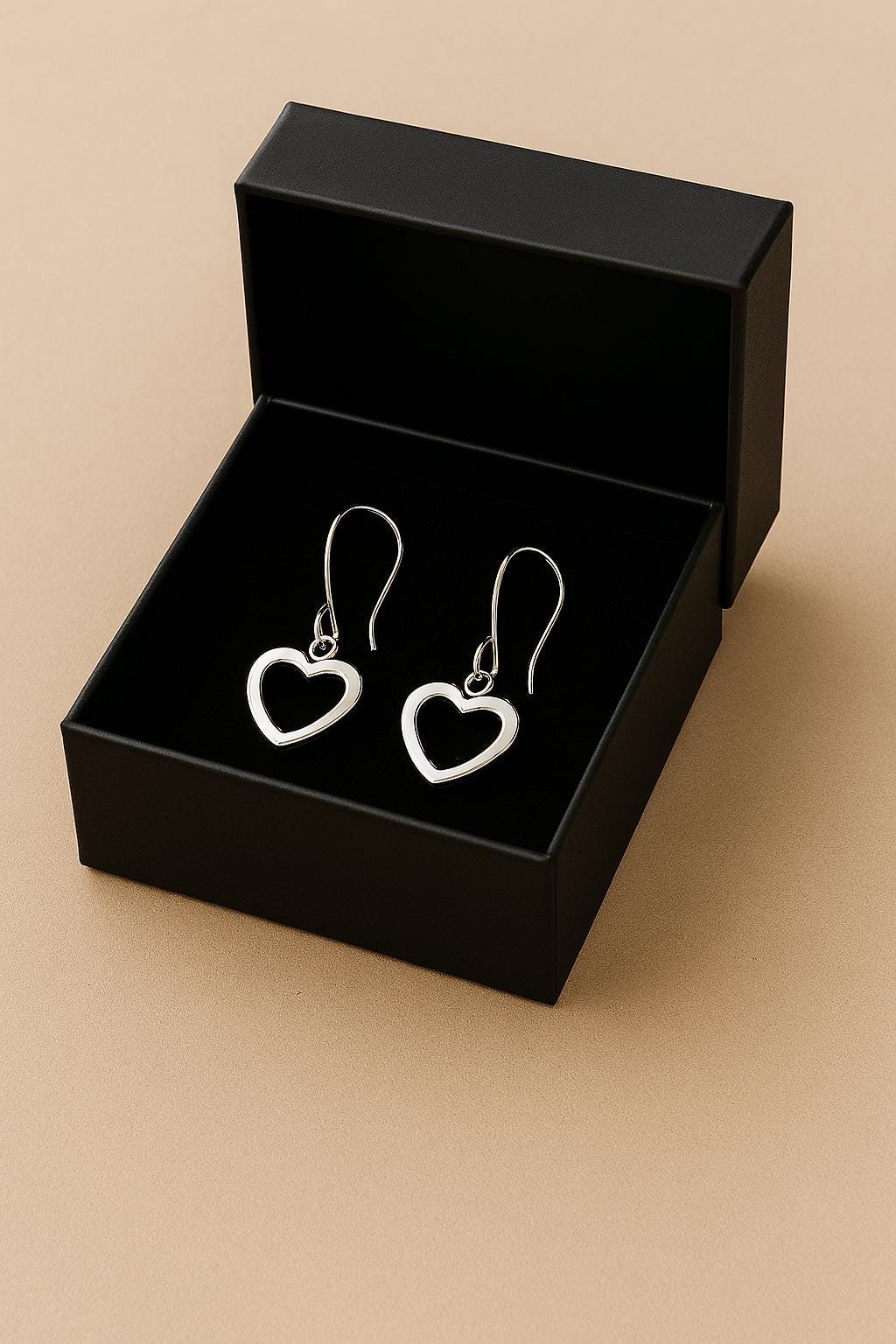 Heart-shaped earrings in a black box on a beige background