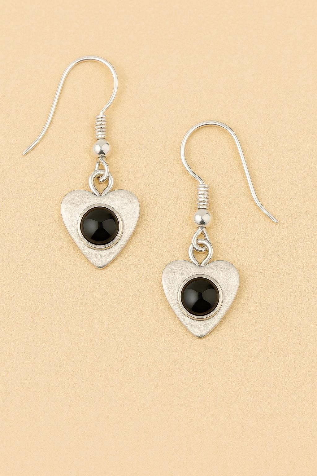Heart-shaped earrings with black stones on a beige background