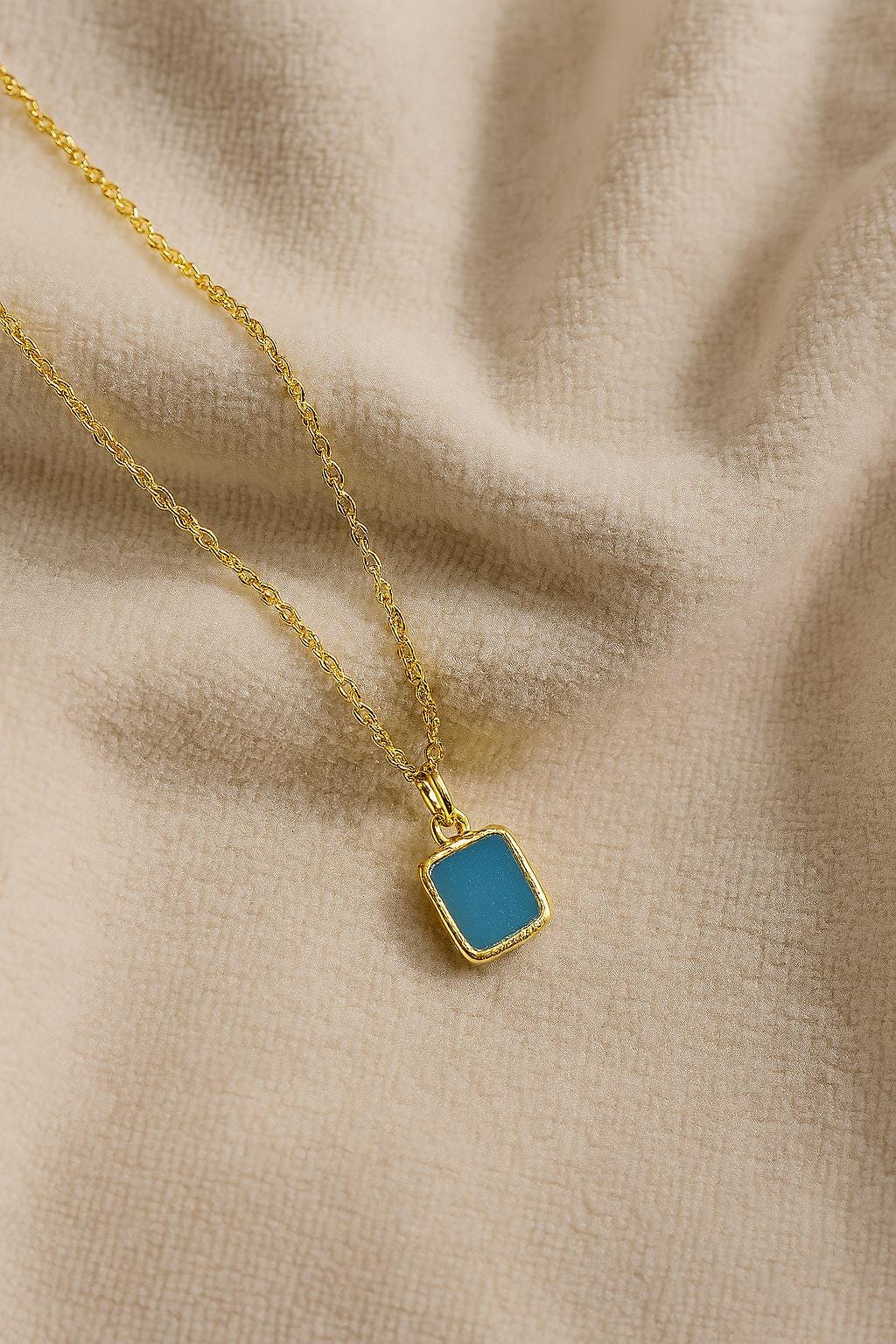 Gold necklace with a blue pendant on a beige fabric background