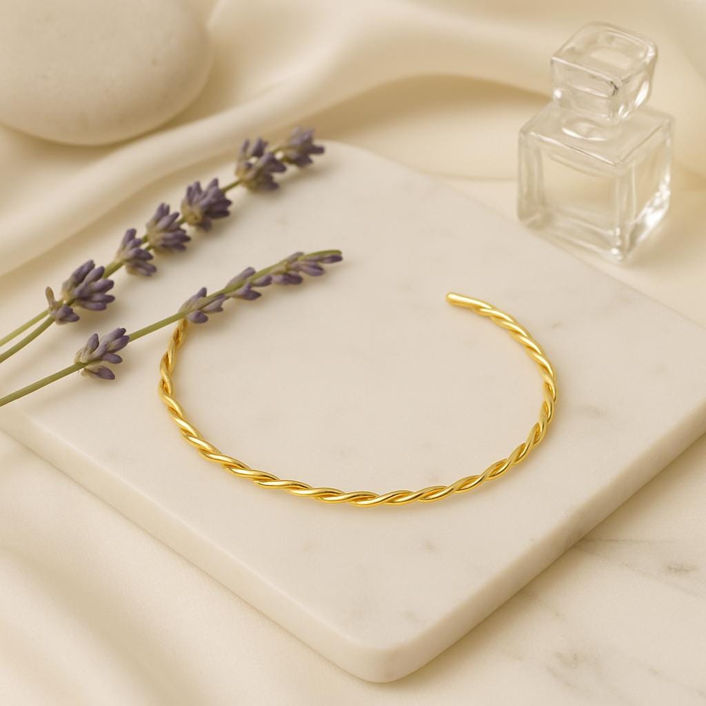 Gold bracelet on a marble surface with lavender and a glass container.