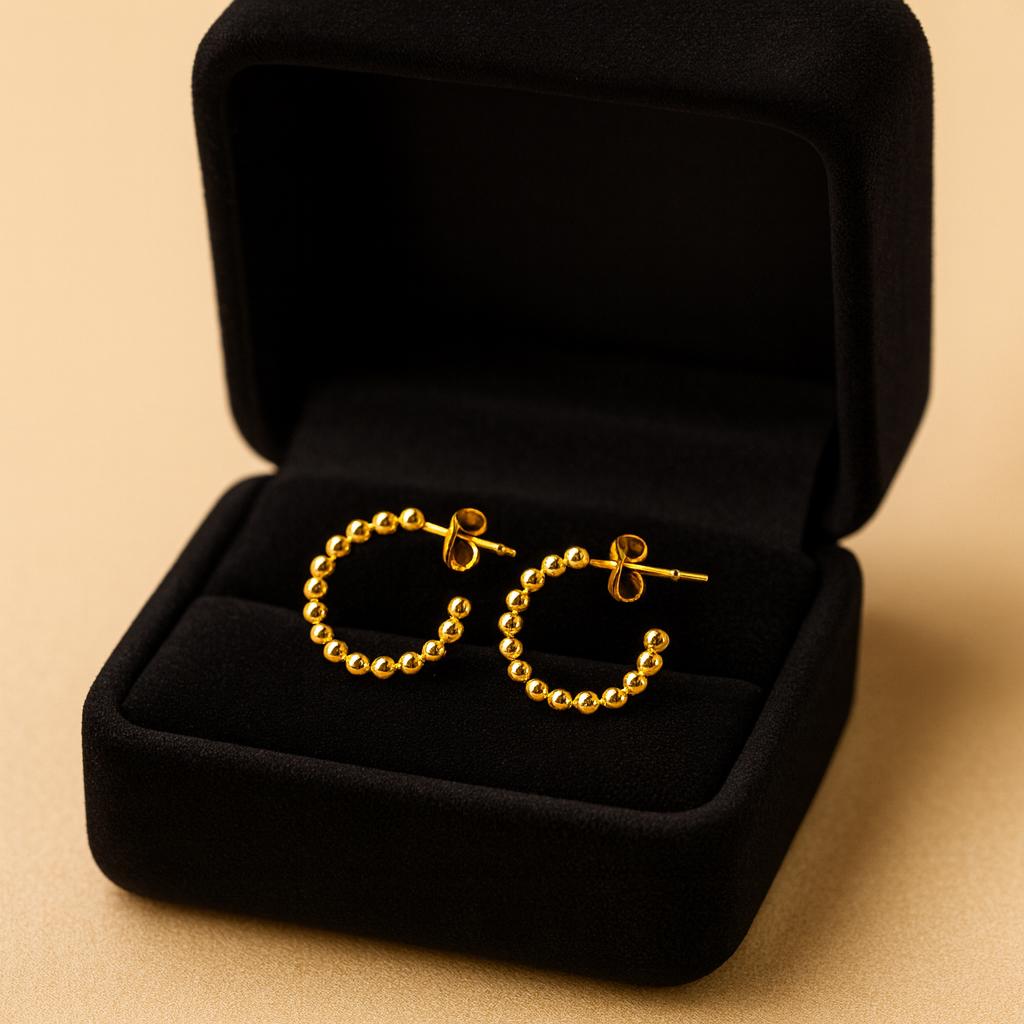 Gold hoop earrings in a black jewelry box on a beige background