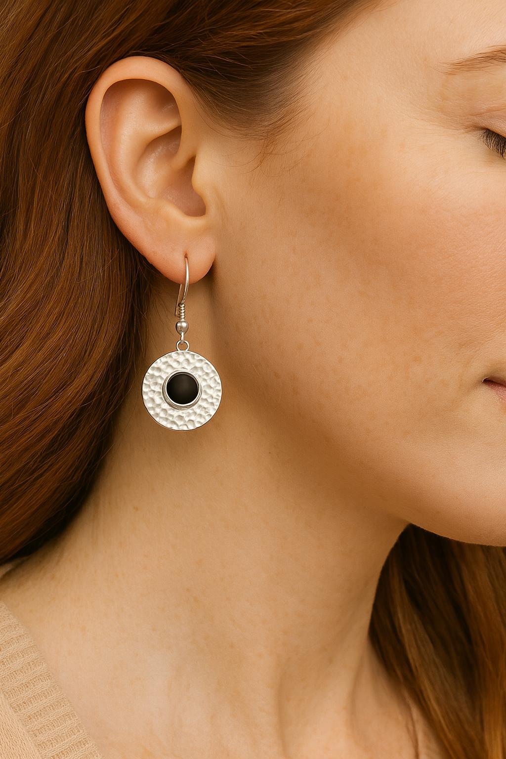 Close-up of a person wearing a silver earring with a black gemstone.