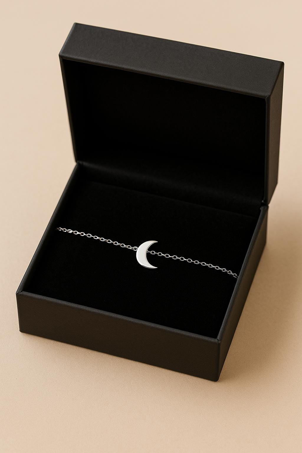 Black jewelry box with a silver bracelet featuring a moon charm on a beige background