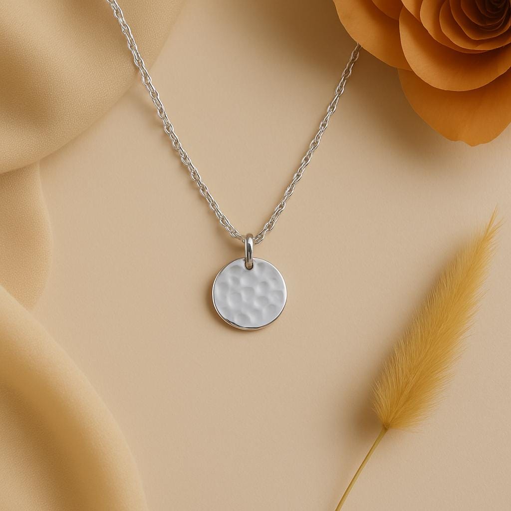 Silver necklace with a round pendant on a beige background with flowers and grass.