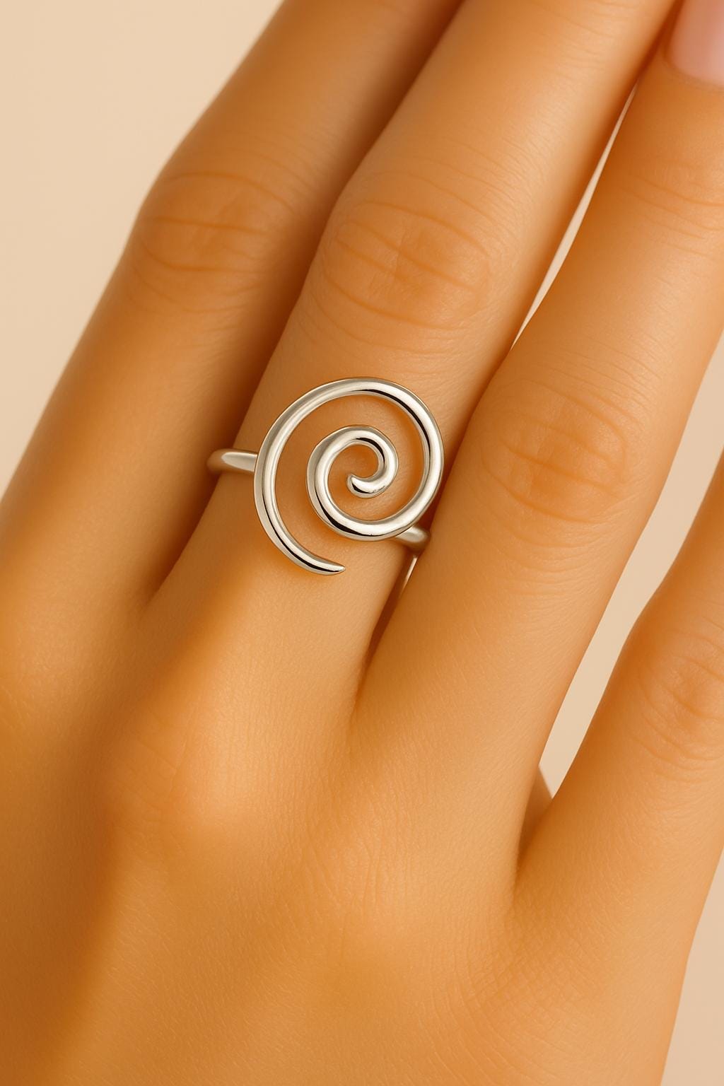 Silver spiral ring on a hand against a beige background