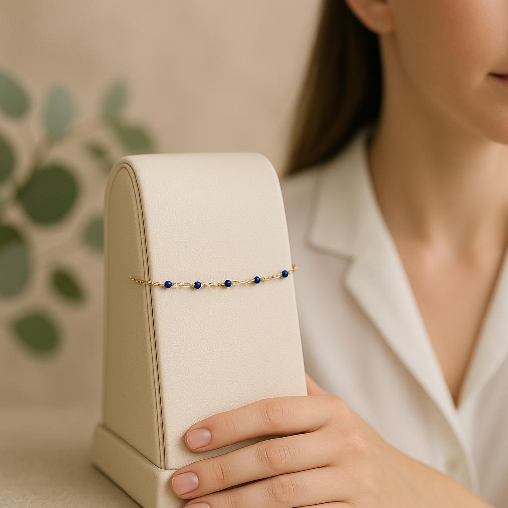Woman holding a gold and blue beaded bracelet on a beige stand with a blurred green leafy background