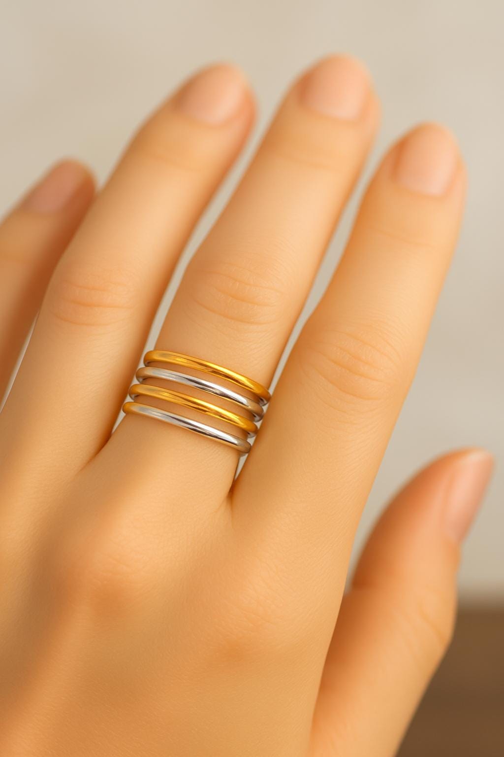 Hand wearing a gold and silver ring on a neutral background