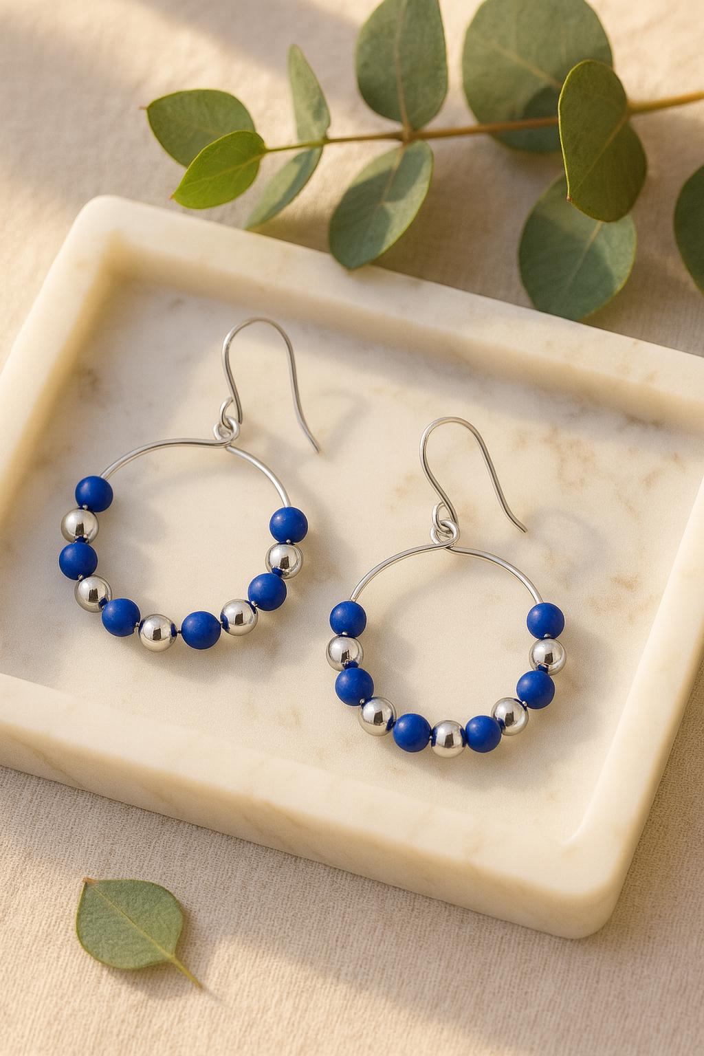 Hoop earrings with blue and silver beads on a marble tray with green leaves.