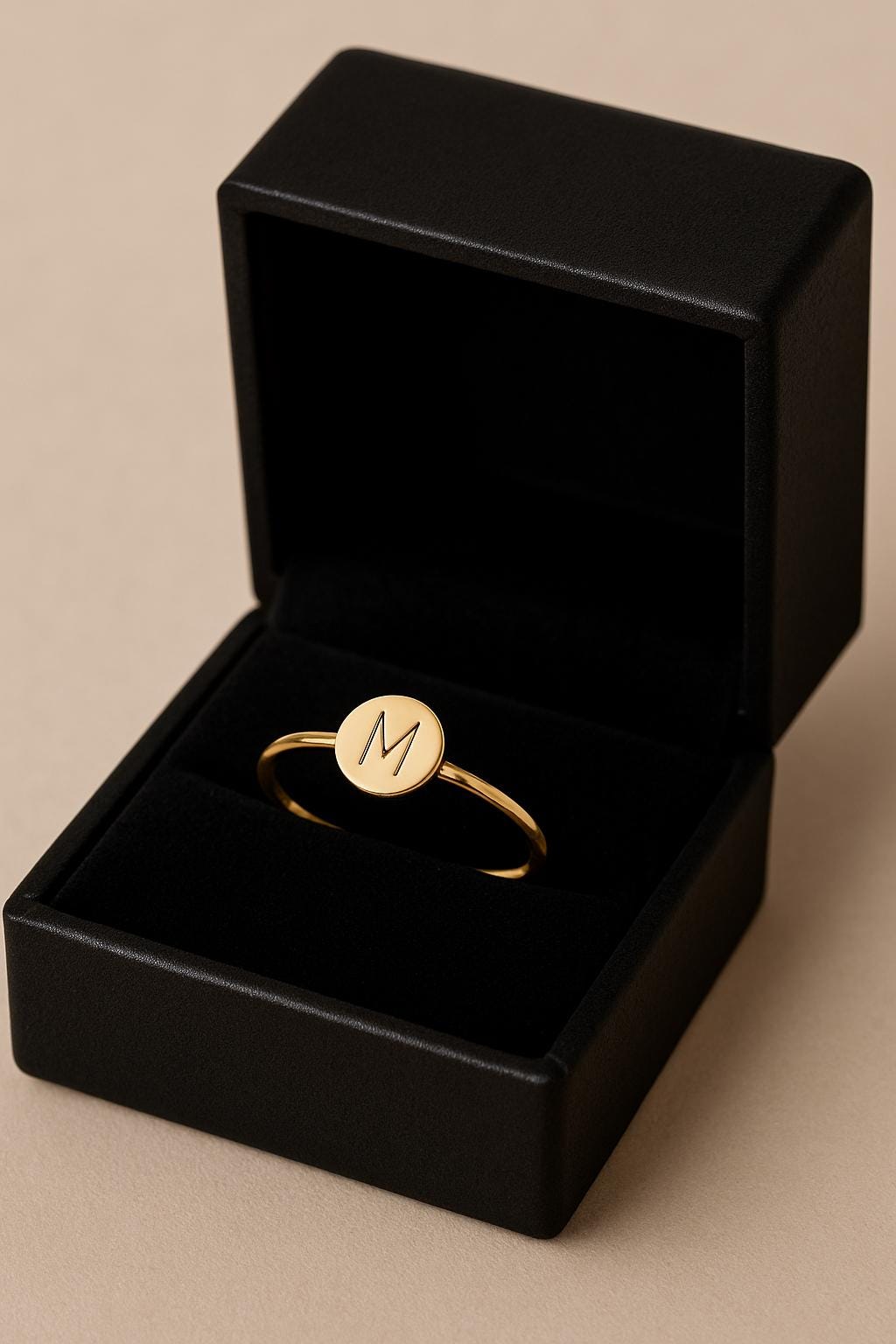 Gold ring with a monogram in a black jewelry box on a beige background