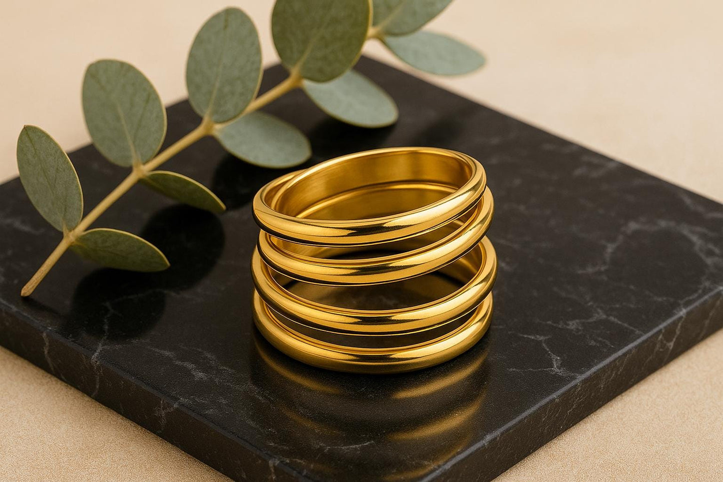 Stack of gold rings on a black marble surface with green leaves.