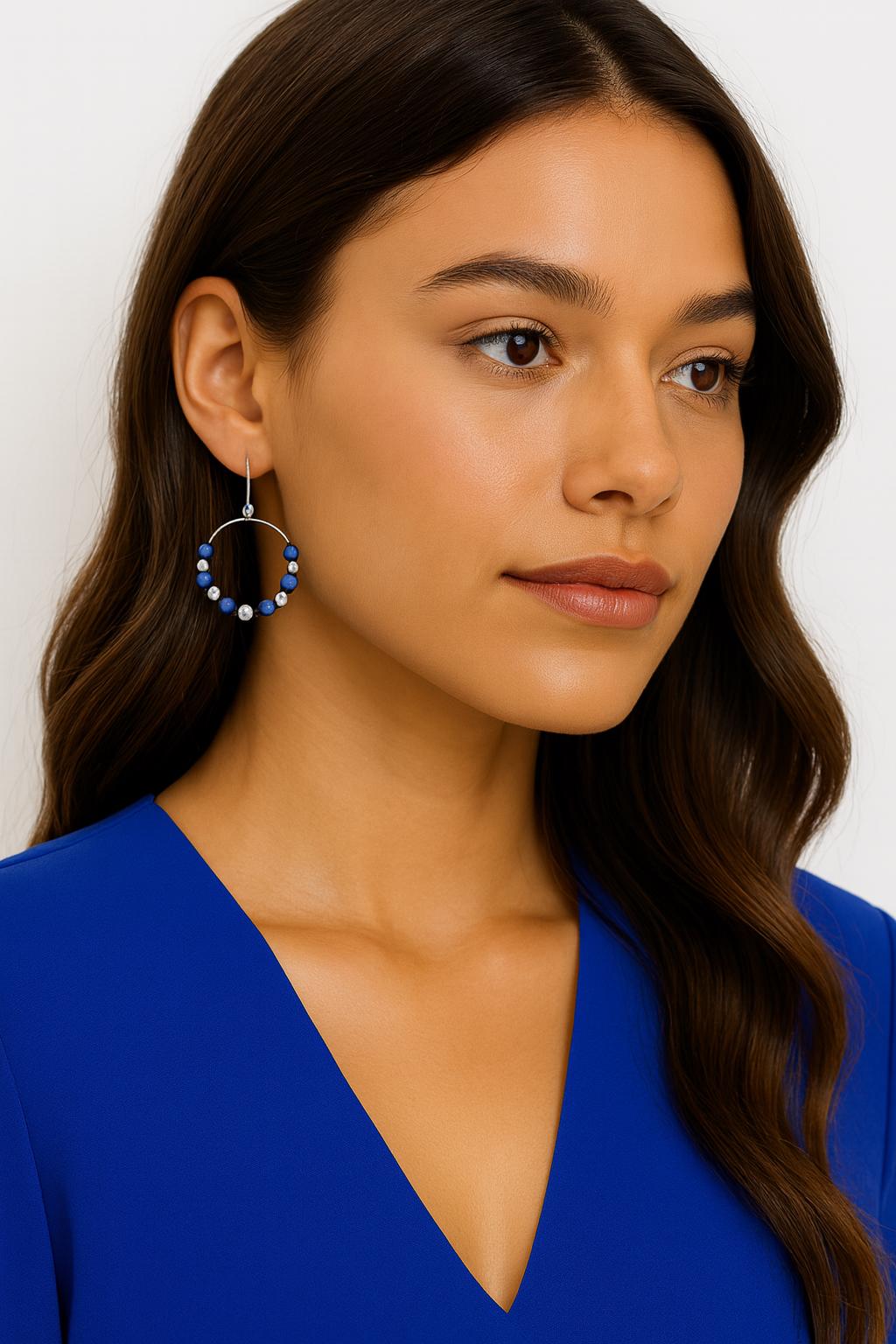 Woman wearing a blue top and hoop earrings with a neutral background