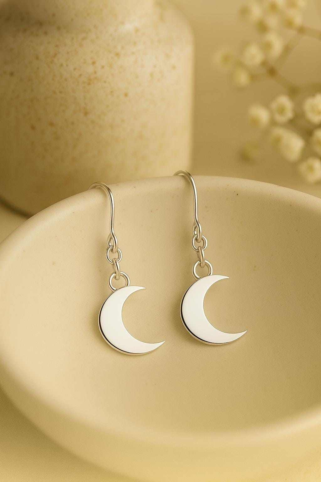 Silver moon-shaped earrings on a beige surface with a blurred background