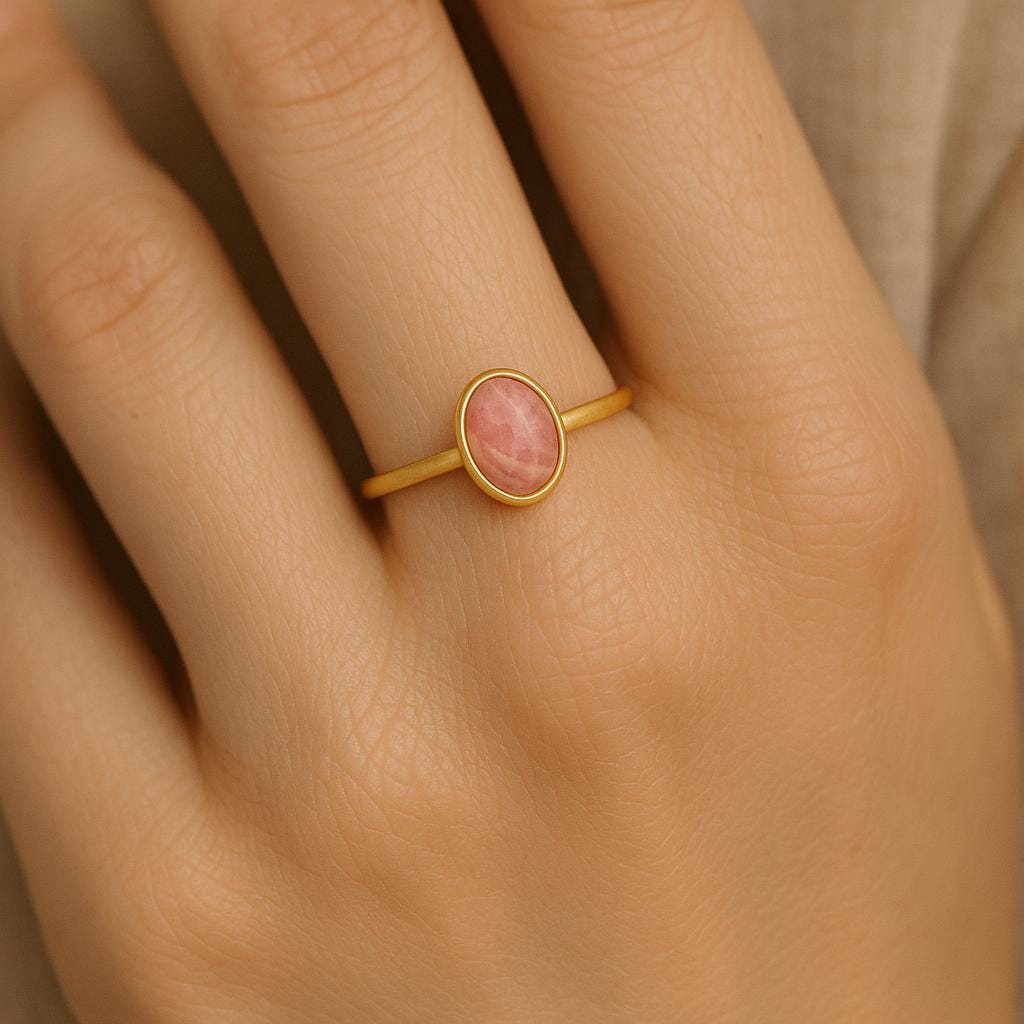 Gold ring with a pink stone on a hand against a neutral background
