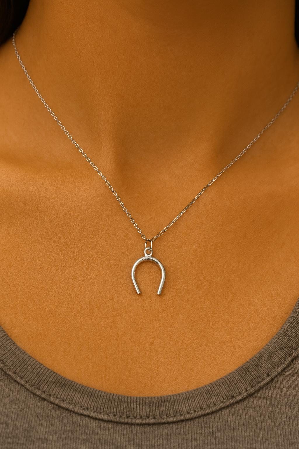 Silver horseshoe necklace on a person wearing a brown shirt.