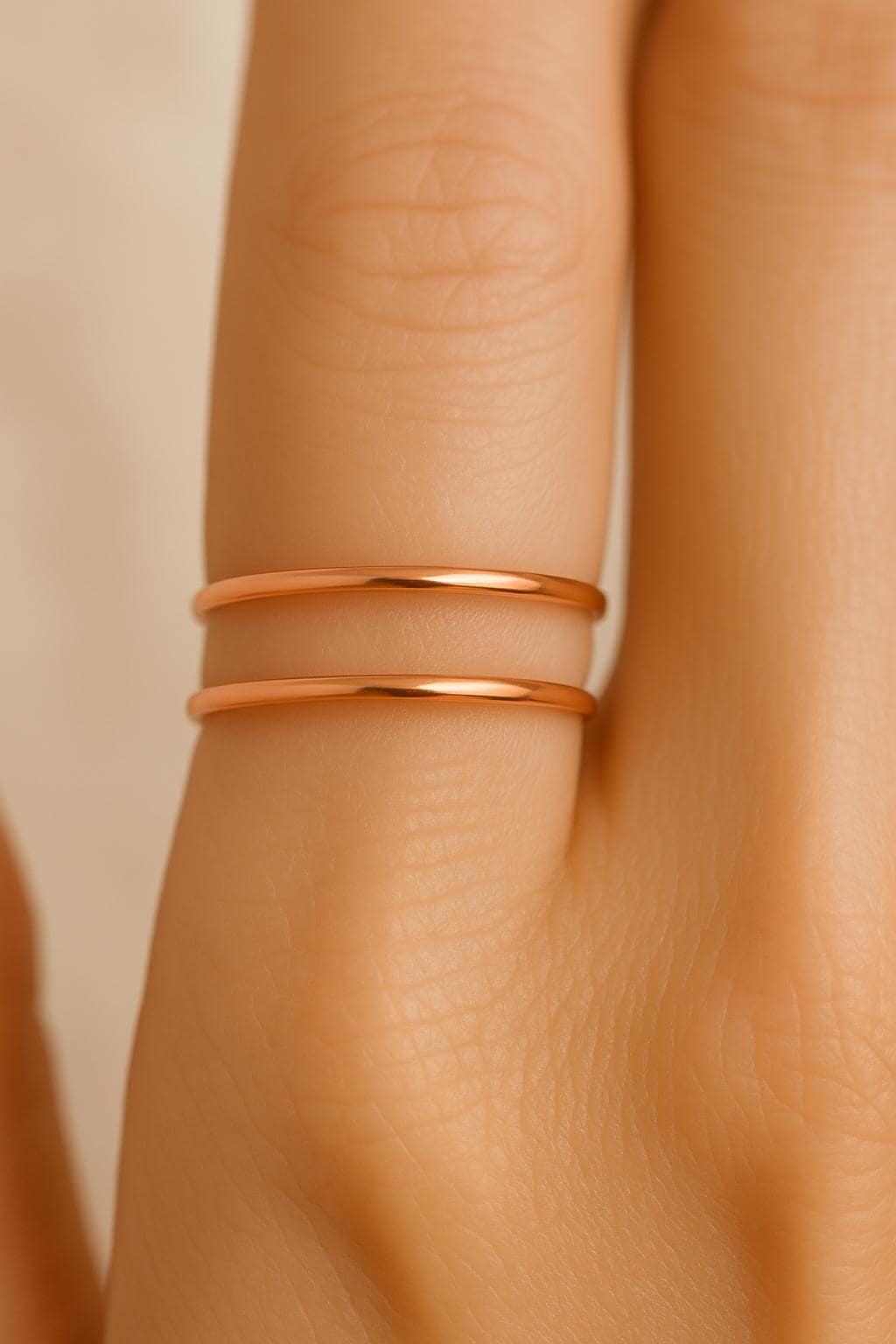 Close-up of a person's wrist wearing two rose gold bracelets on a beige background