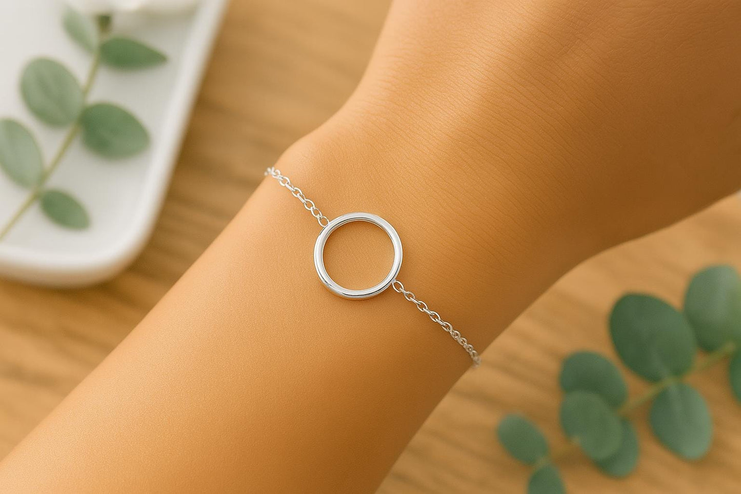 Silver bracelet with a circular design on a wrist, with green leaves in the background.