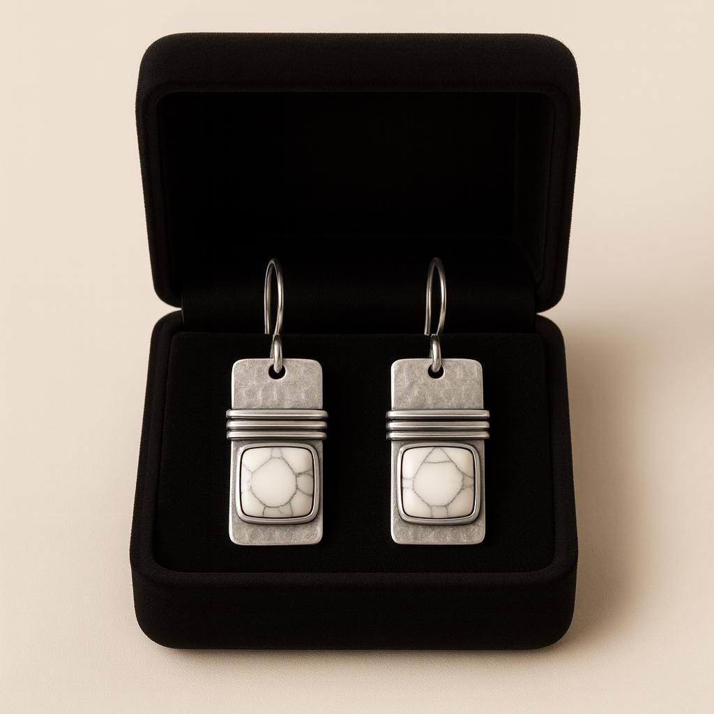 Pair of silver earrings with a textured design in a black jewelry box on a beige background