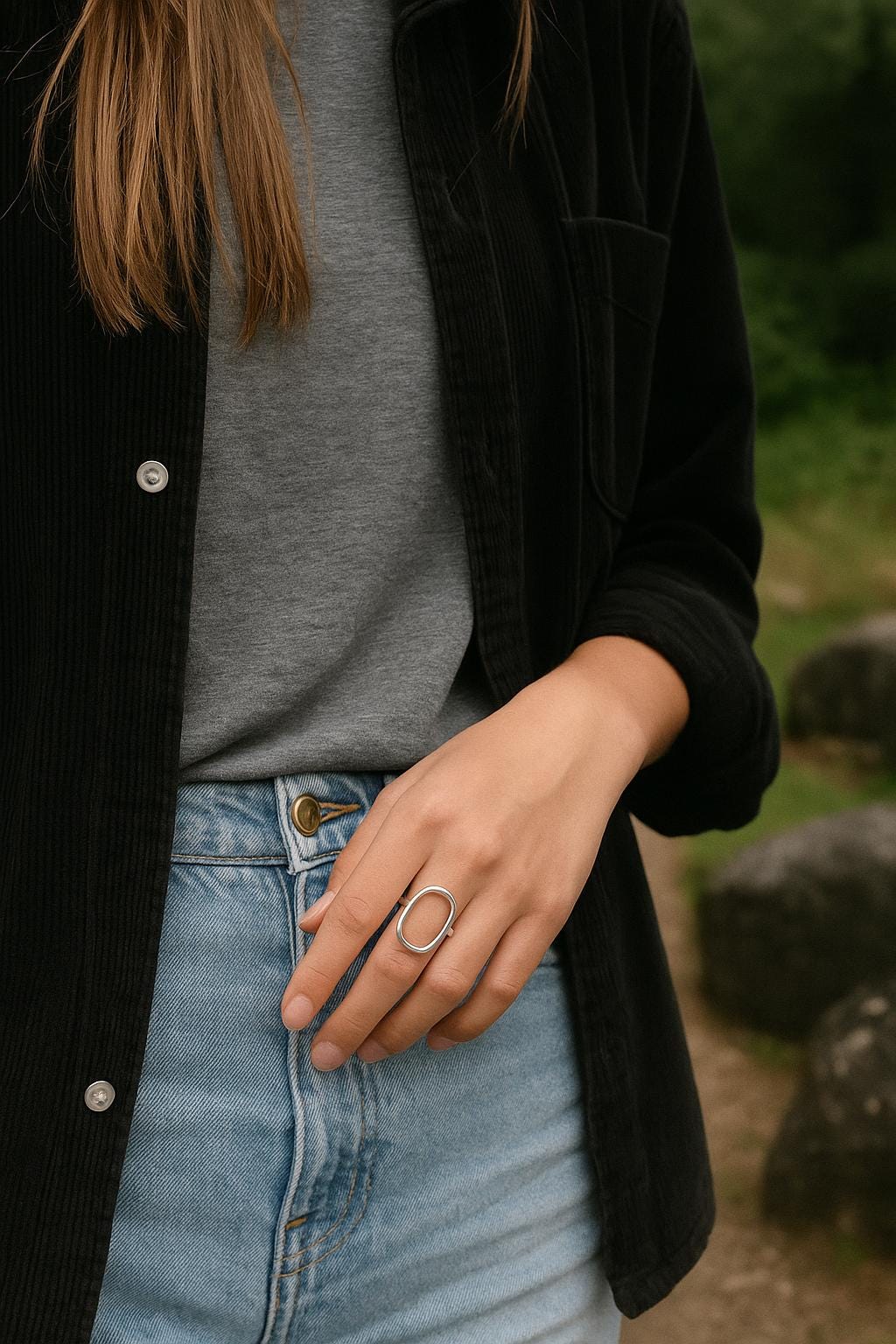 Person wearing a black jacket, gray shirt, and blue jeans with a blurred natural background