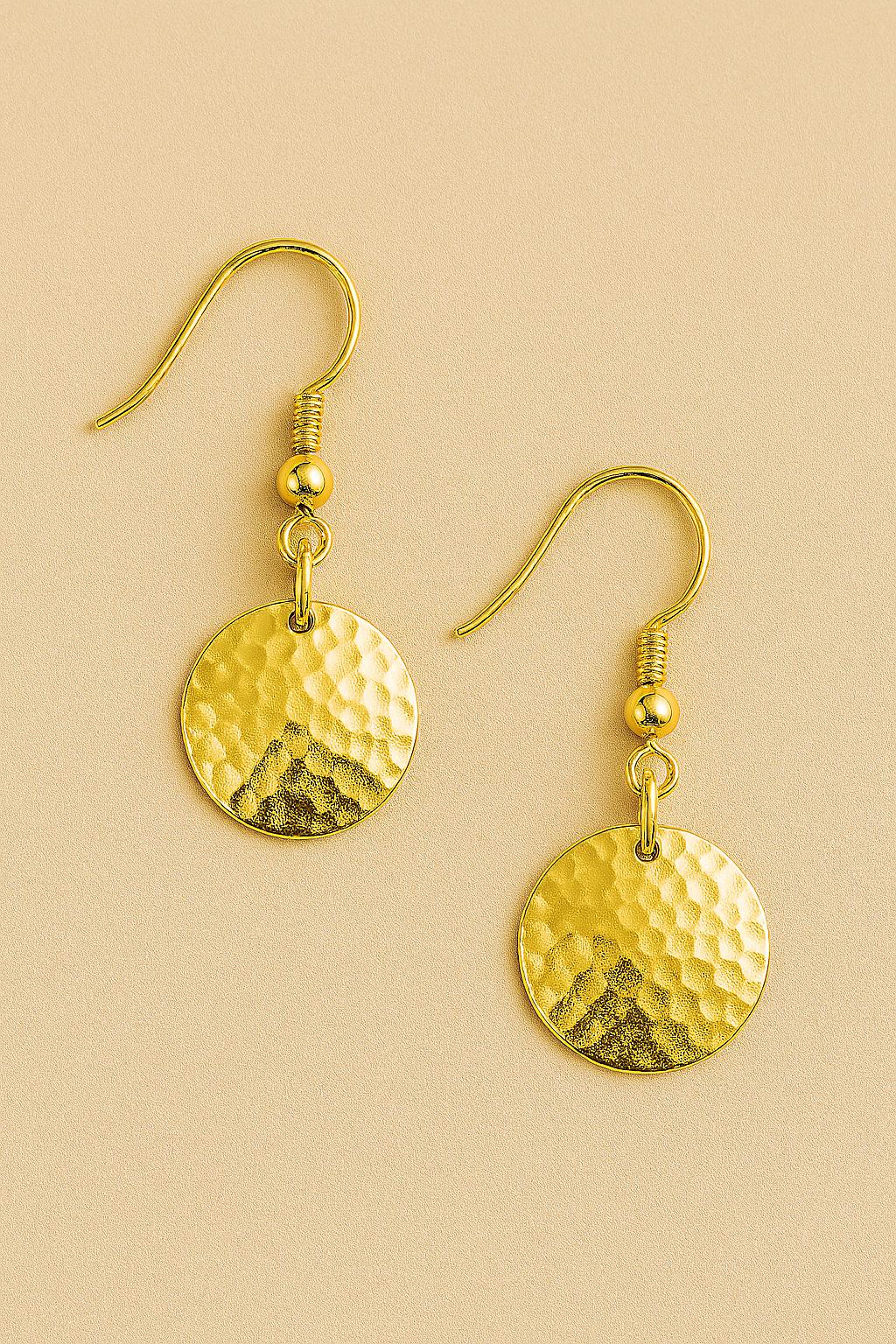 Gold earrings with textured round discs on a beige background