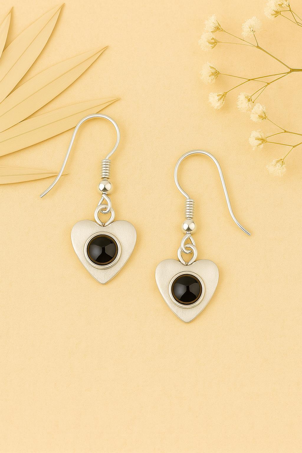 Heart-shaped earrings with black stones on a yellow background