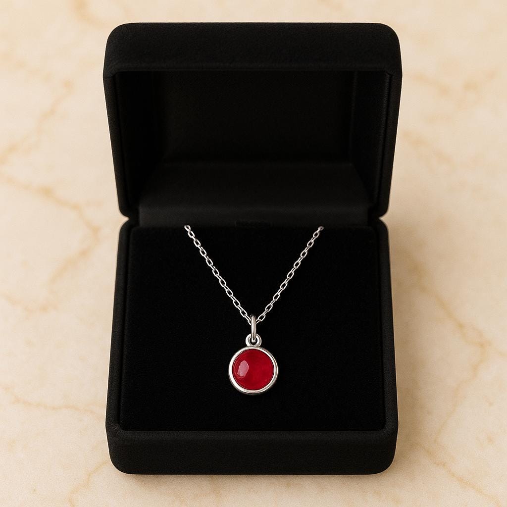 Necklace with a red pendant in a black jewelry box on a beige surface