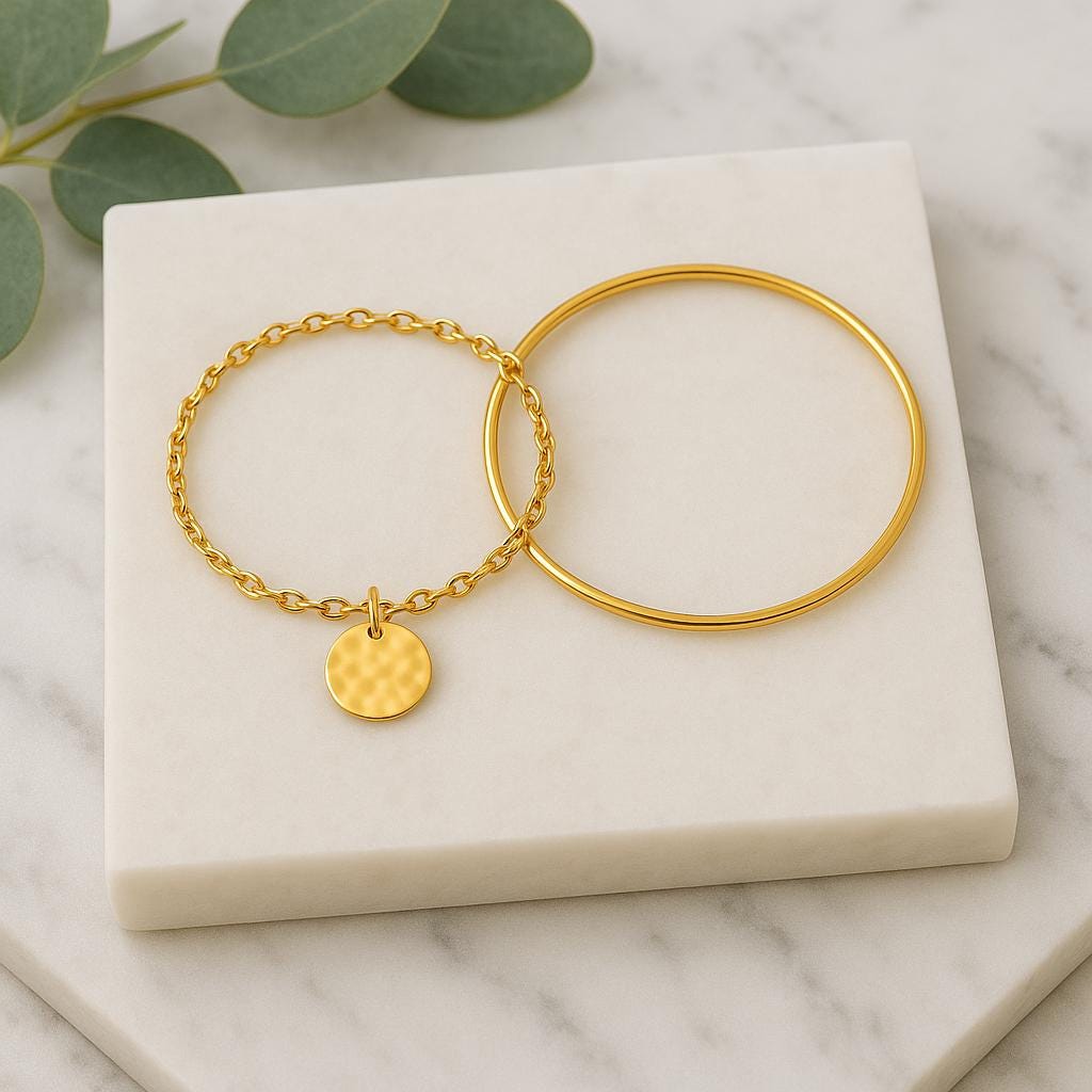 Two gold bracelets on a marble surface with green leaves.