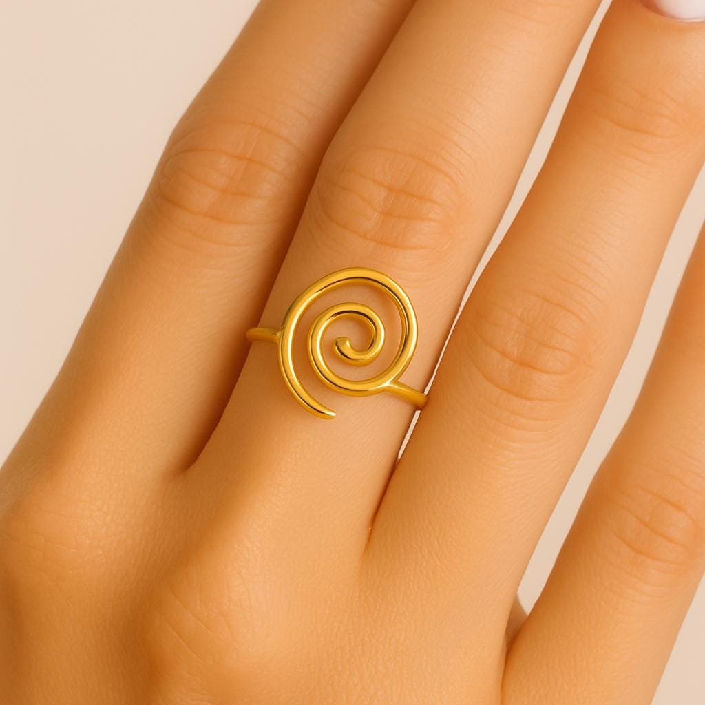 Gold spiral ring on a person's finger against a neutral background
