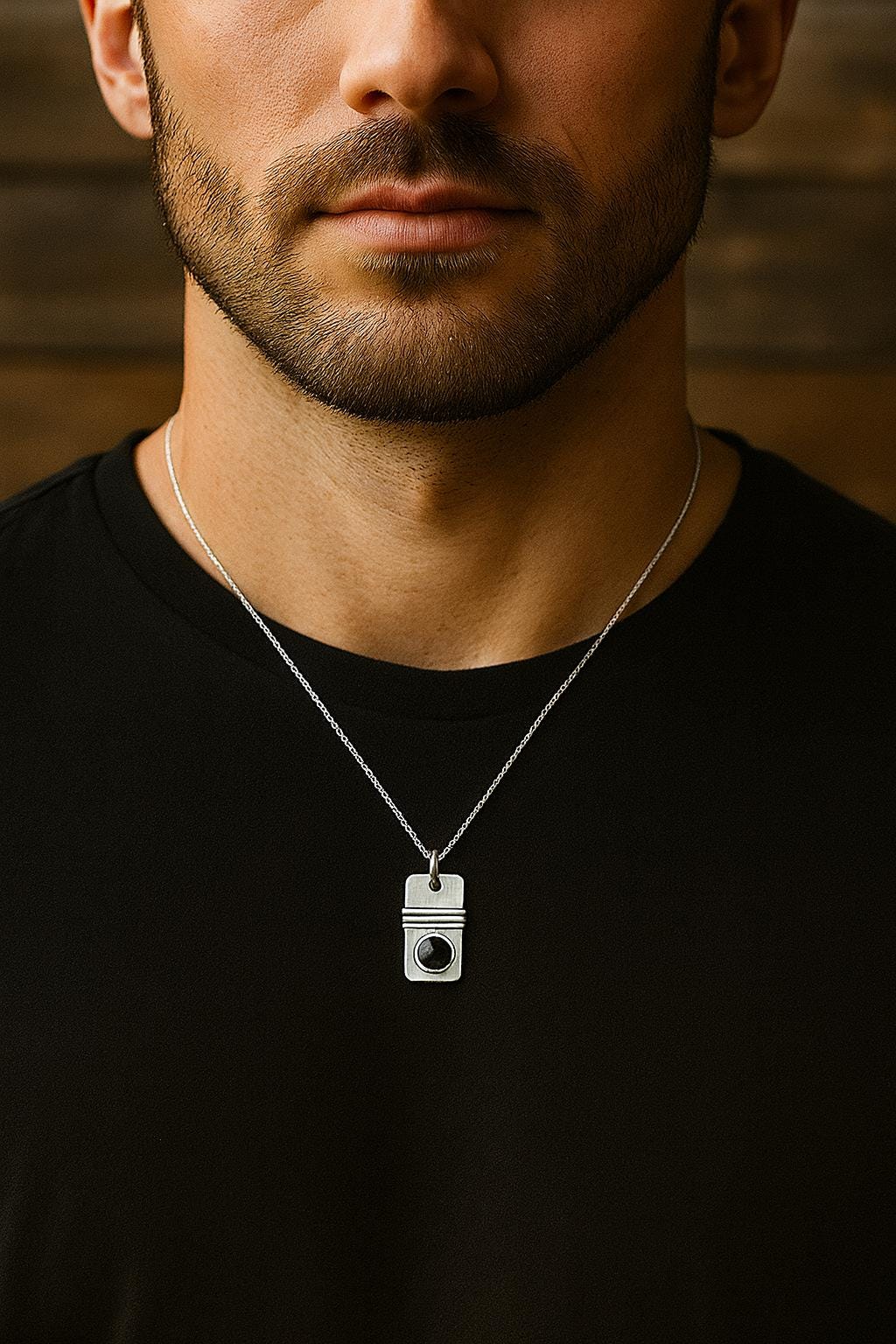 Man wearing a black shirt with a silver necklace featuring a camera pendant against a wooden background