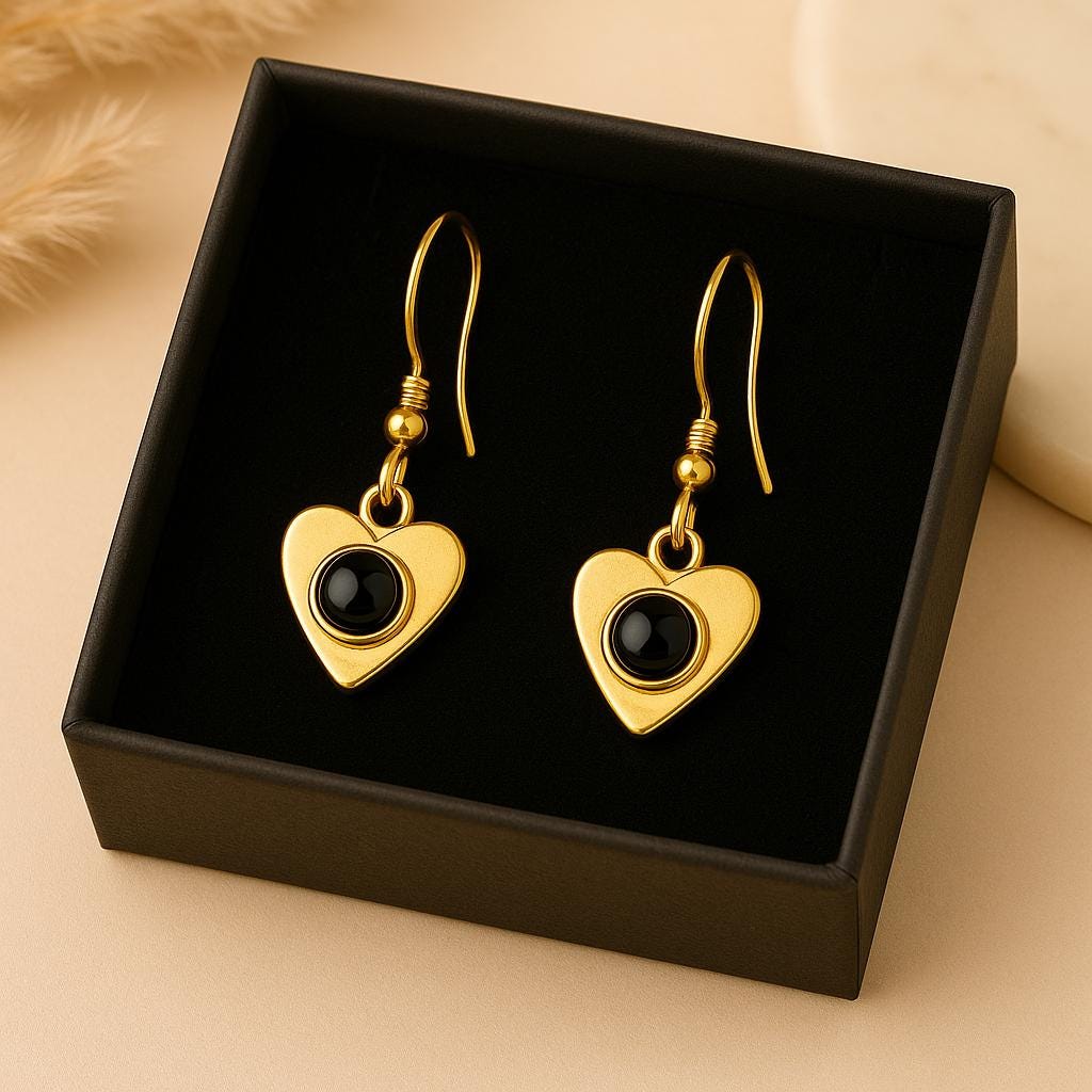Gold heart-shaped earrings with black stones in a black box on a beige background