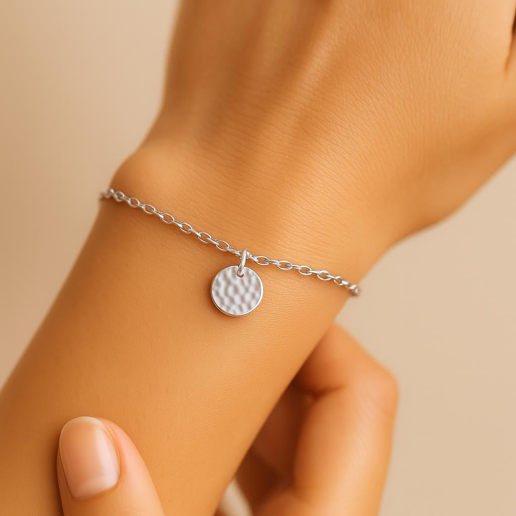 Silver bracelet with a round charm on a wrist against a beige background