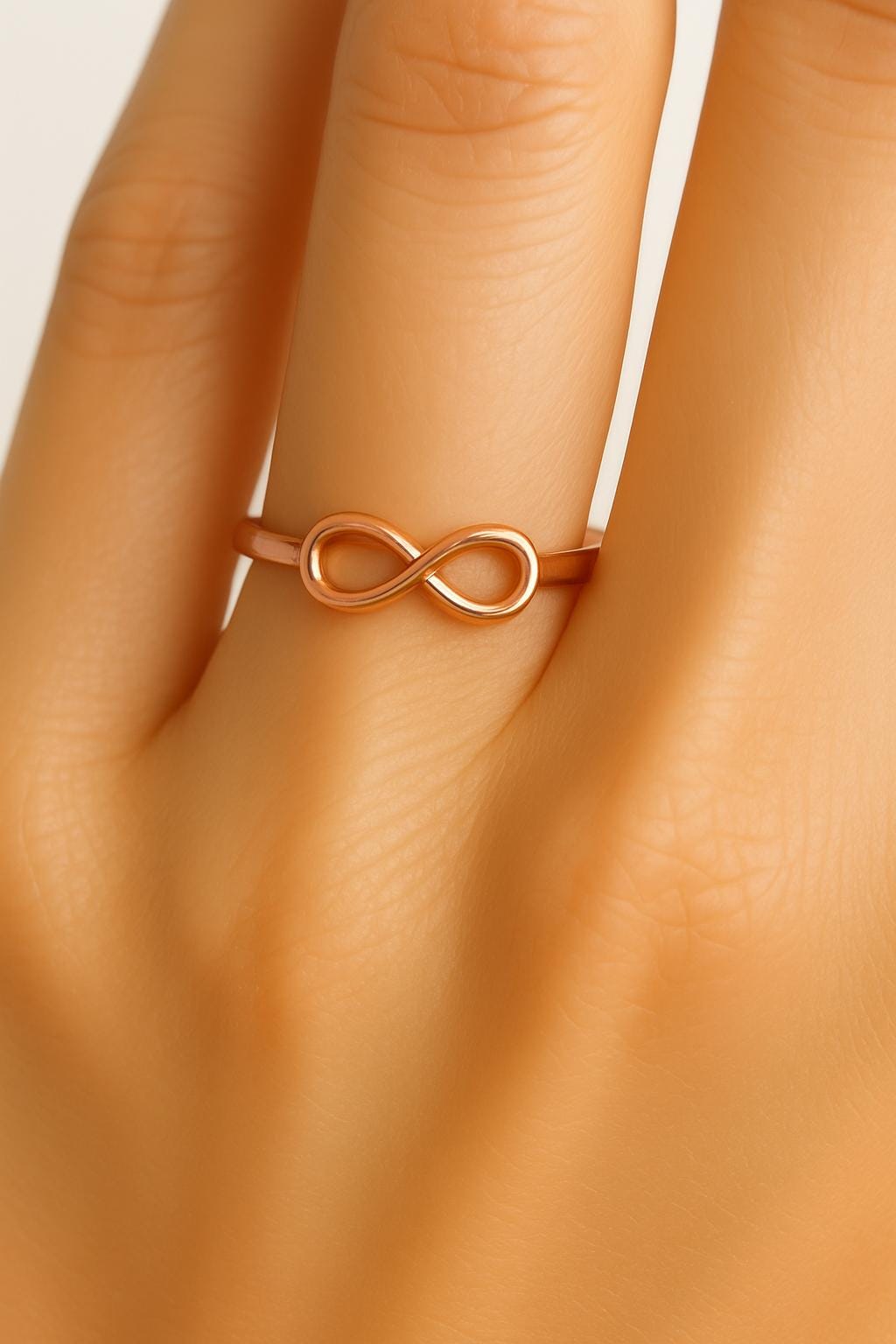 Rose gold infinity ring on a hand against a white background