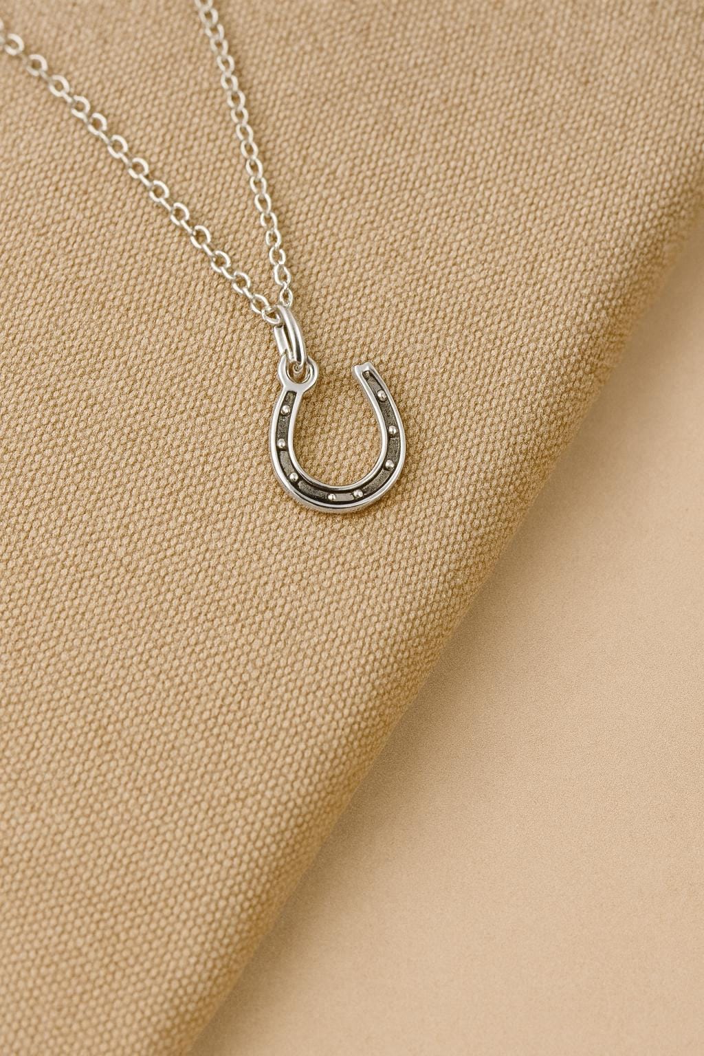 Silver horseshoe necklace on a beige fabric background