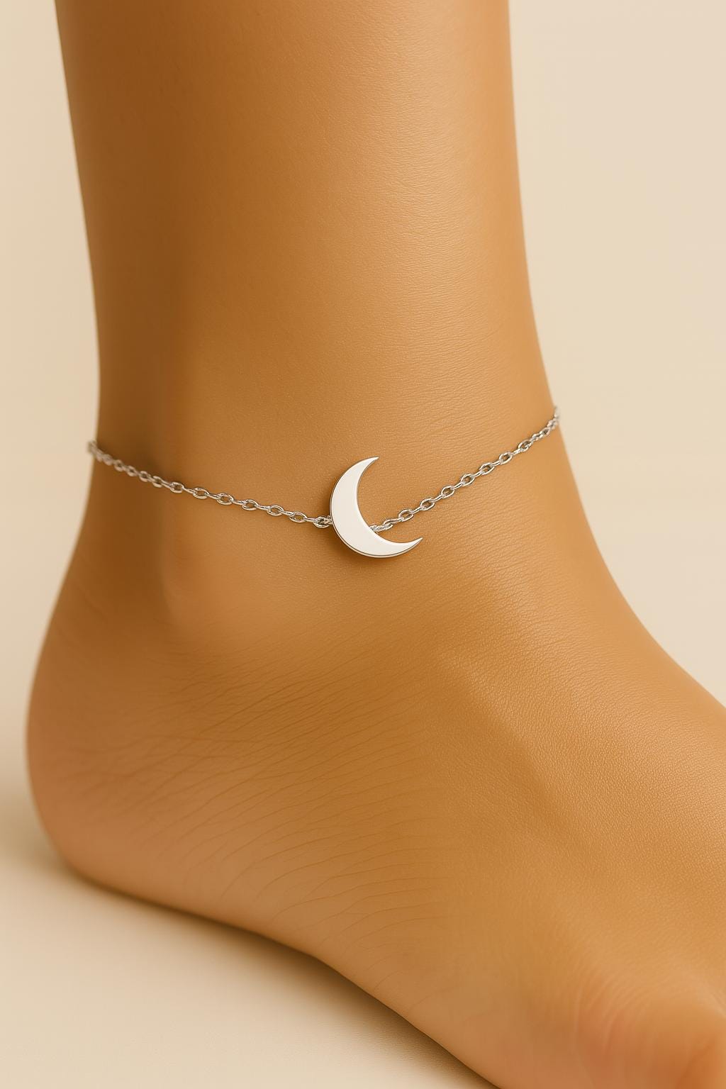 Silver crescent moon anklet on a foot against a beige background