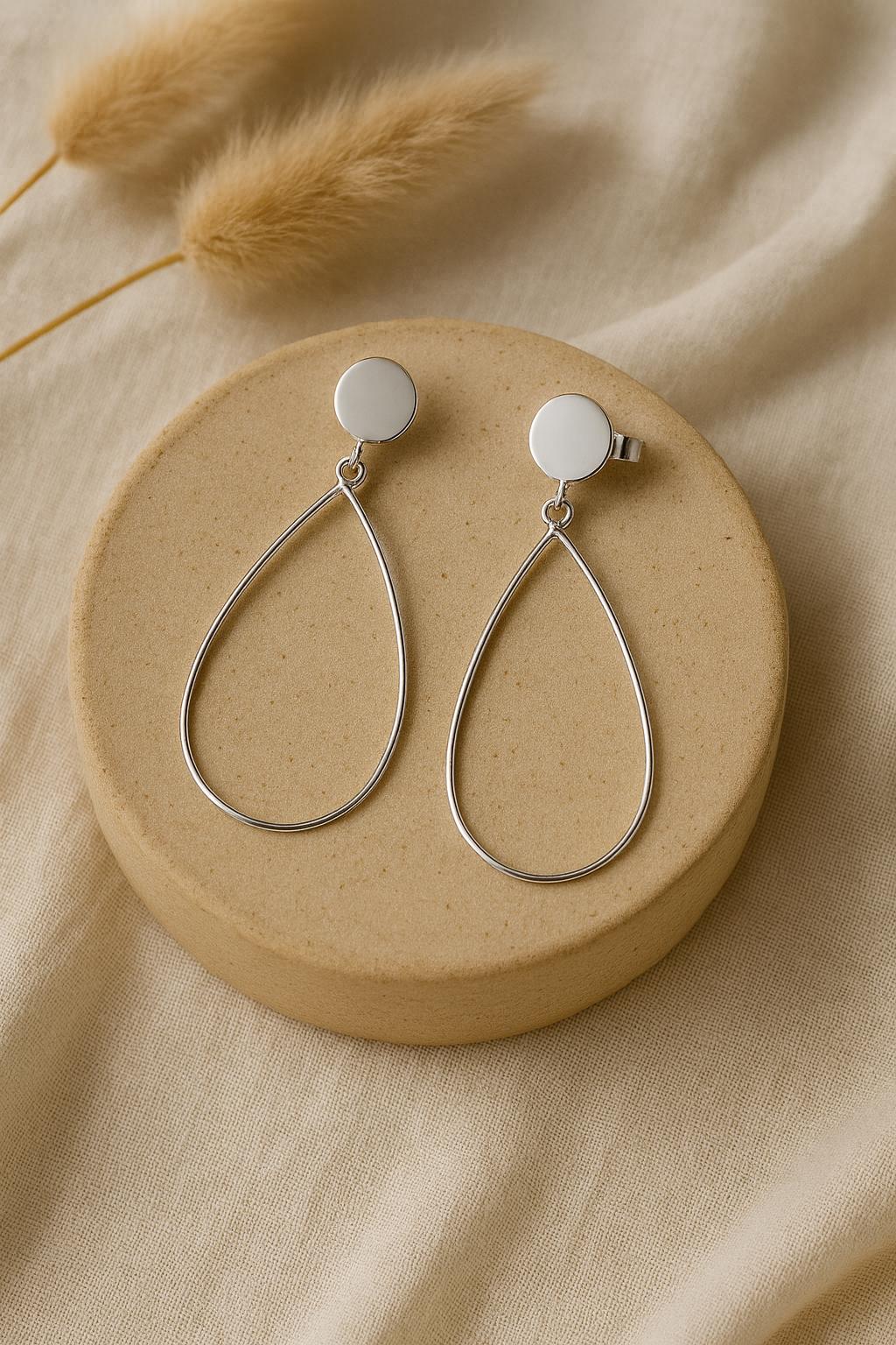 Silver teardrop earrings on a beige circular stand with dried pampas grass.