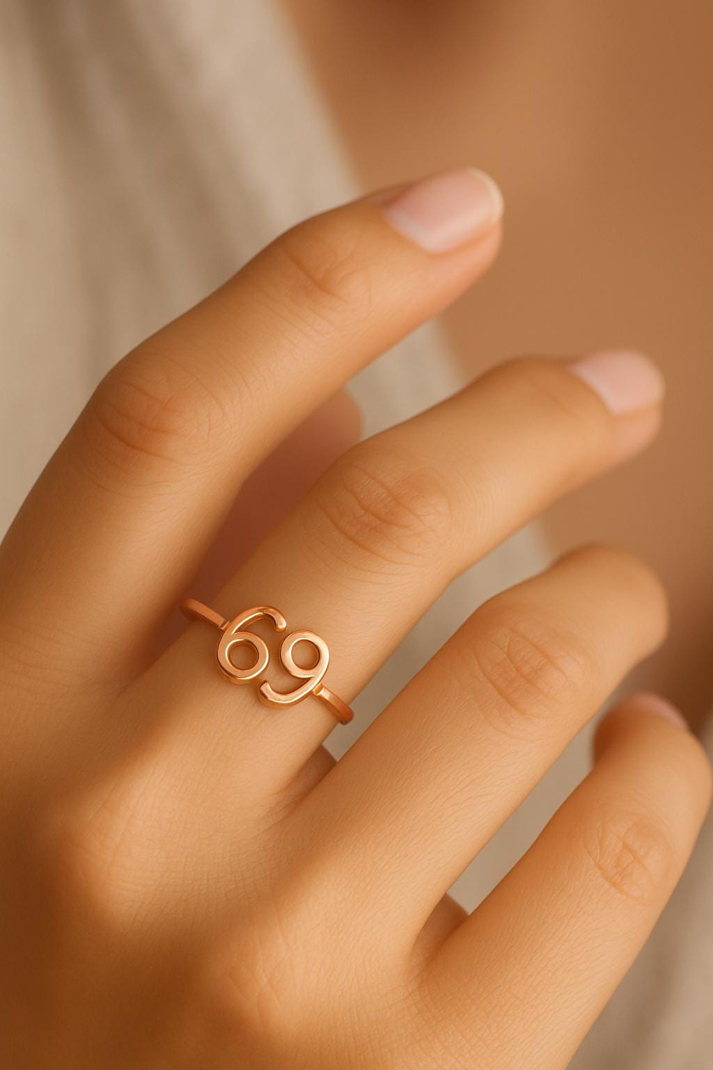 Rose gold ring with the number '69' on a hand against a neutral background