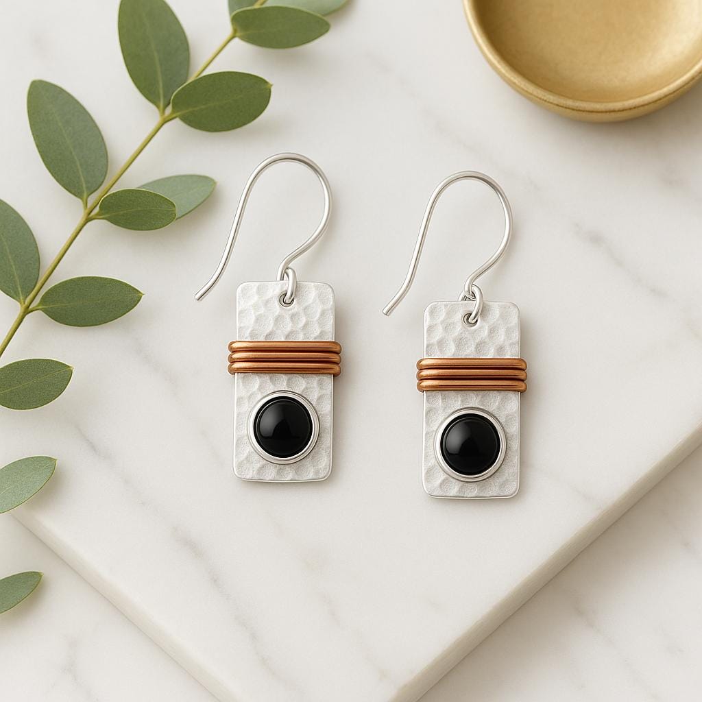 Pair of earrings with black stones and brown accents on a marble surface with green leaves.