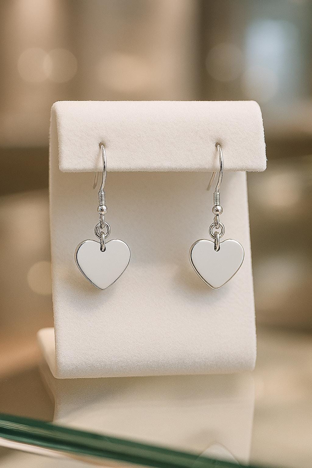Heart-shaped silver earrings on a white earring stand with a blurred background
