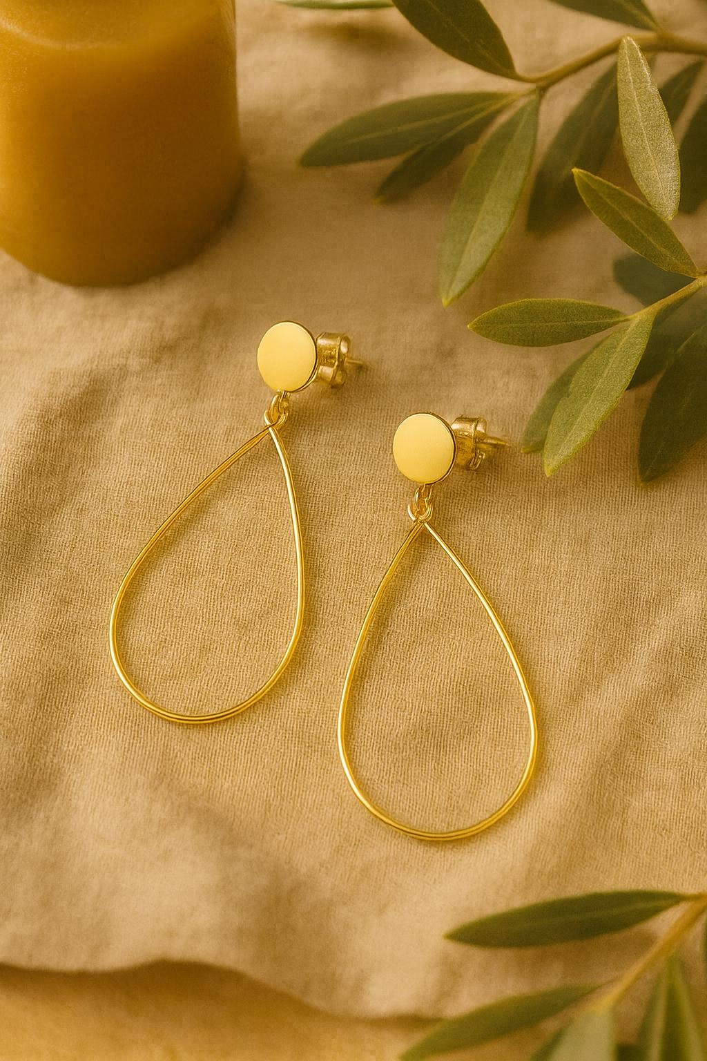 Gold teardrop earrings on a beige fabric background with green leaves.