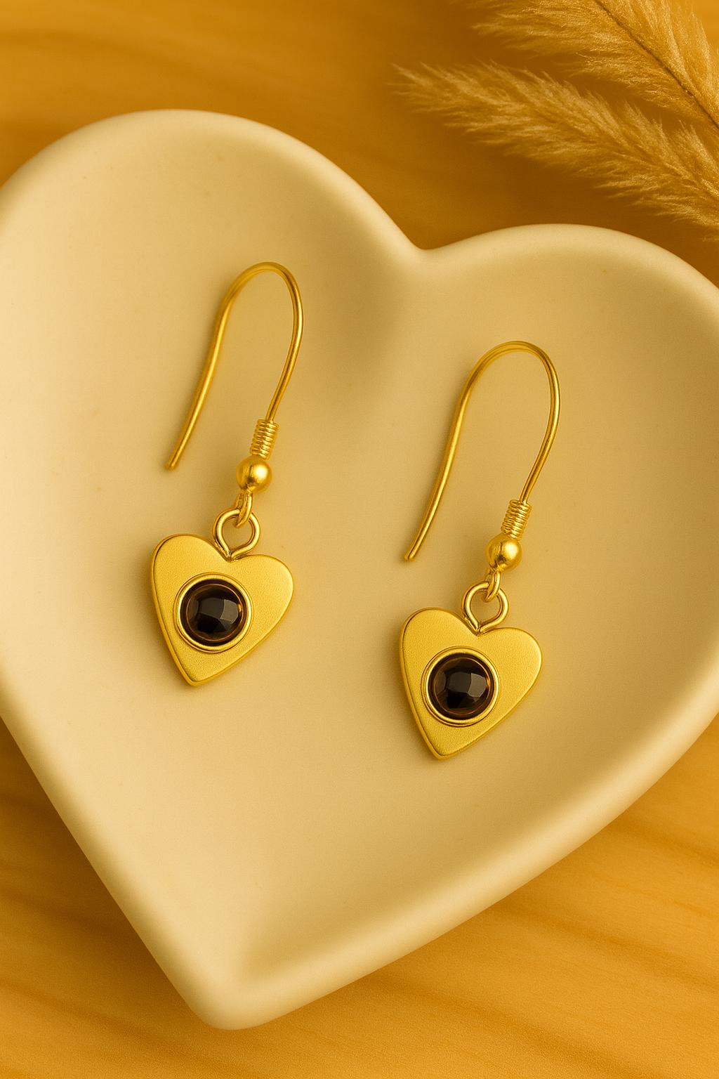 Gold heart-shaped earrings with black stones on a heart-shaped dish.