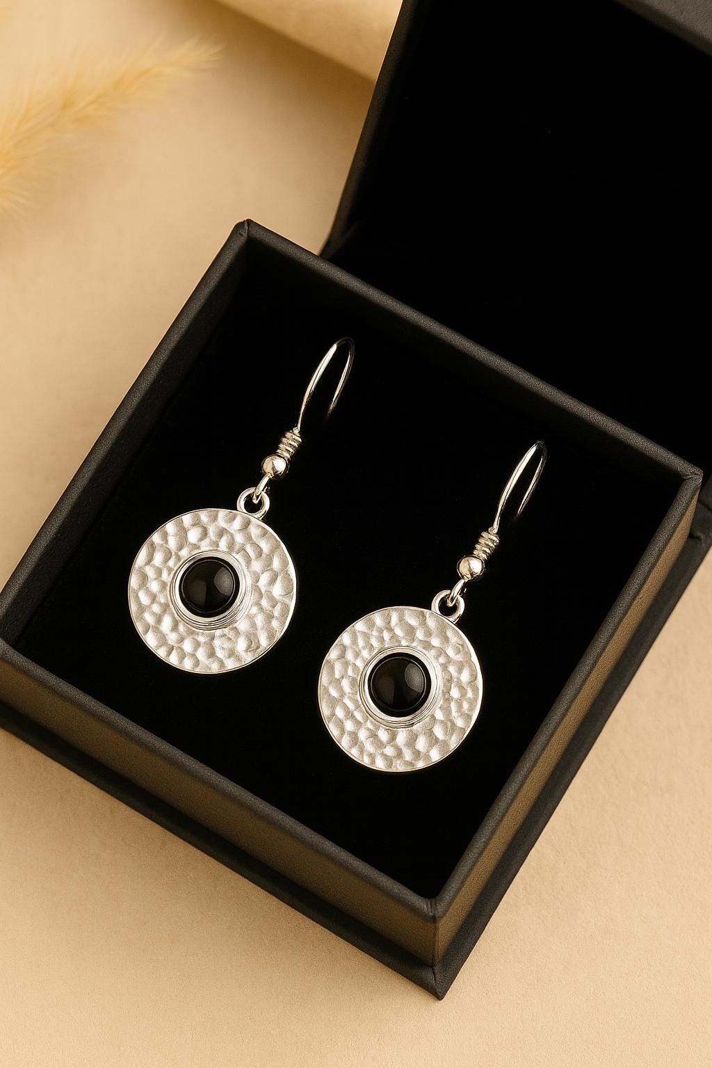 Silver earrings with black centers in a black box on a beige background