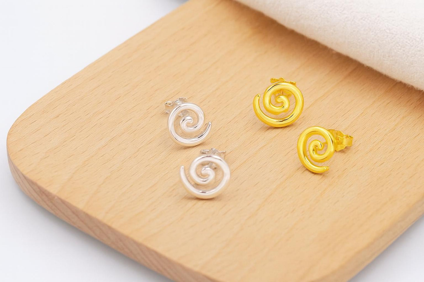 Pair of spiral-shaped earrings, one gold and one silver, on a wooden surface.