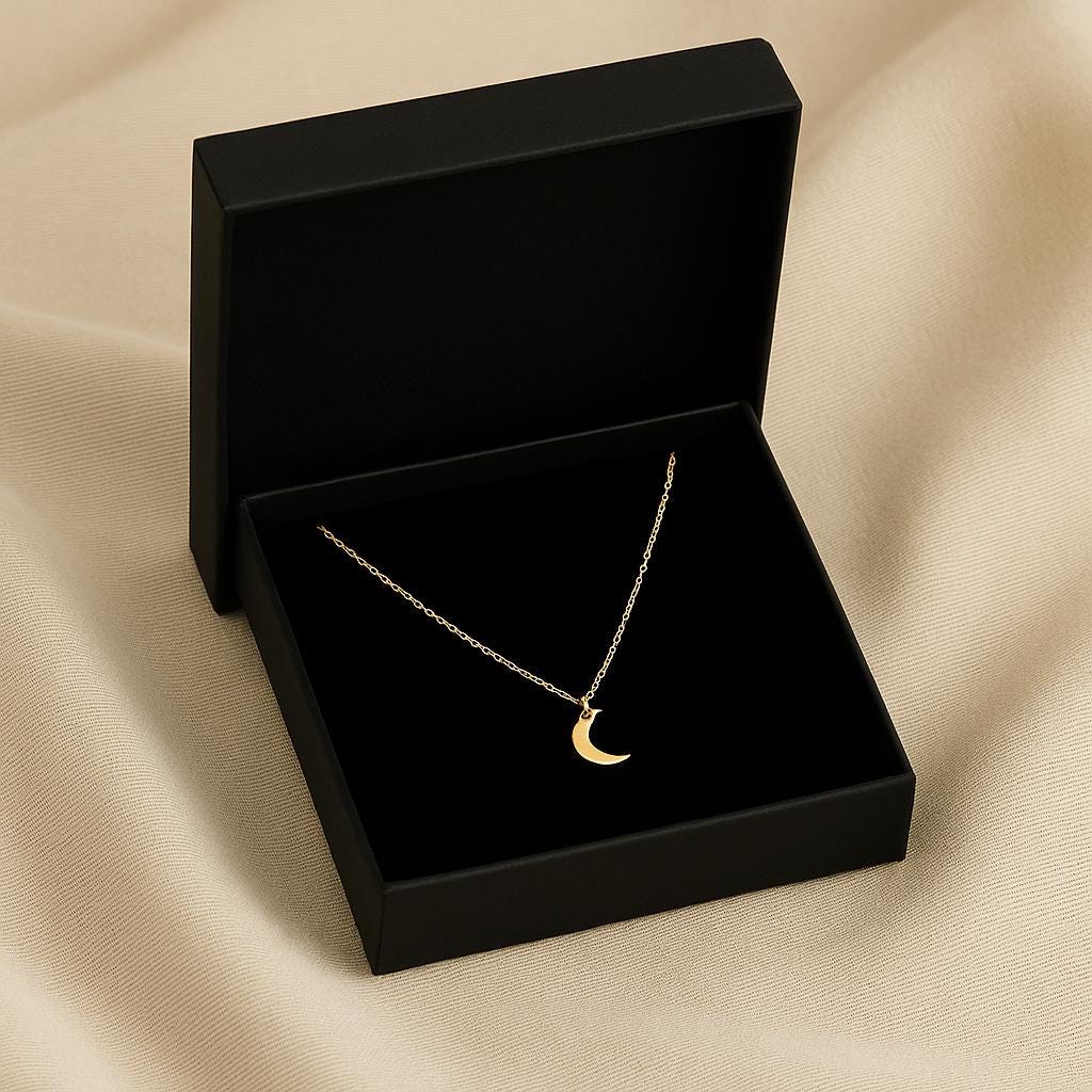 Silver necklace with a crescent moon pendant in a black jewelry box on beige fabric.